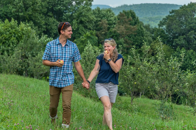 Couple walking through the Orchard at Altapass eating apples.